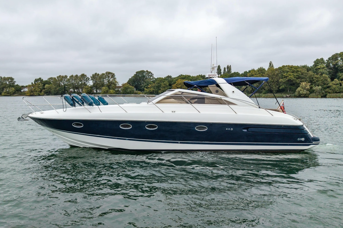 2000 Princess V42 yacht cruising on a calm lake with lush green shoreline.
