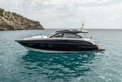 2017 Princess V48 Open yacht on clear blue water near rocky coastline.