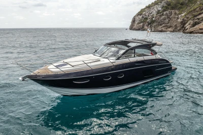 2017 Princess V48 Open yacht cruising near rocky coastline.