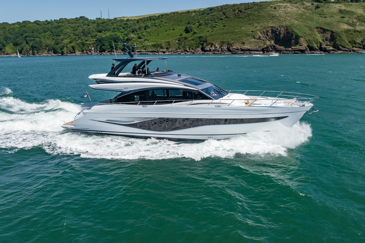 2023 Princess S72 yacht cruising on blue ocean near lush green coastline.