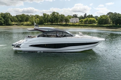 2023 Princess V50 yacht cruising on a serene lake with lush greenery in the background.
