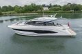 2025 Princess V55 yacht cruising on a serene lake with lush greenery.