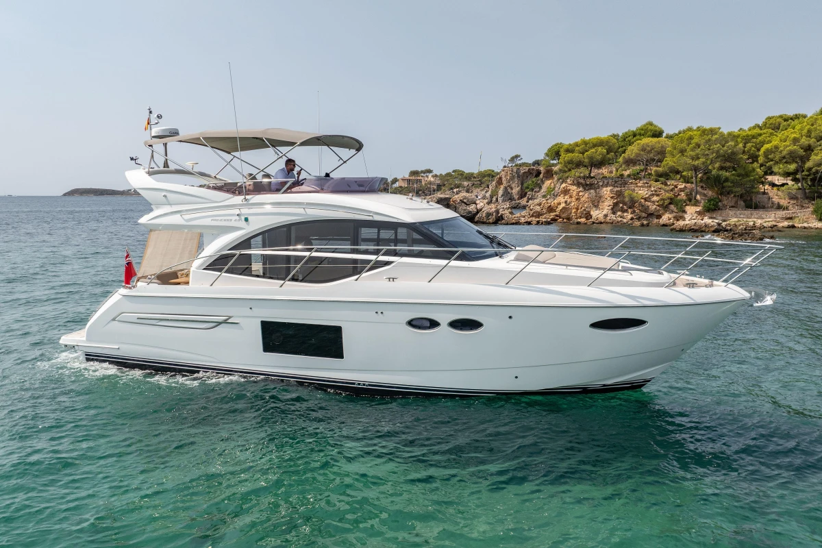 Luxurious 2018 Princess 49 yacht cruising in clear blue waters near a rocky coastline.